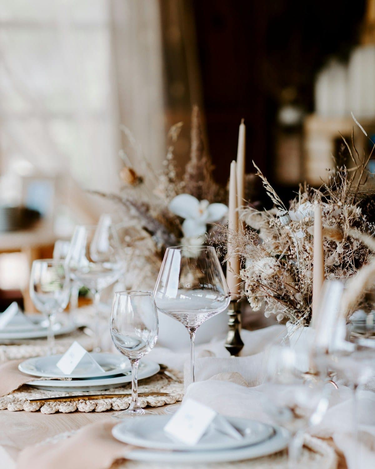Dinner table set with candles, glassware and dried stems