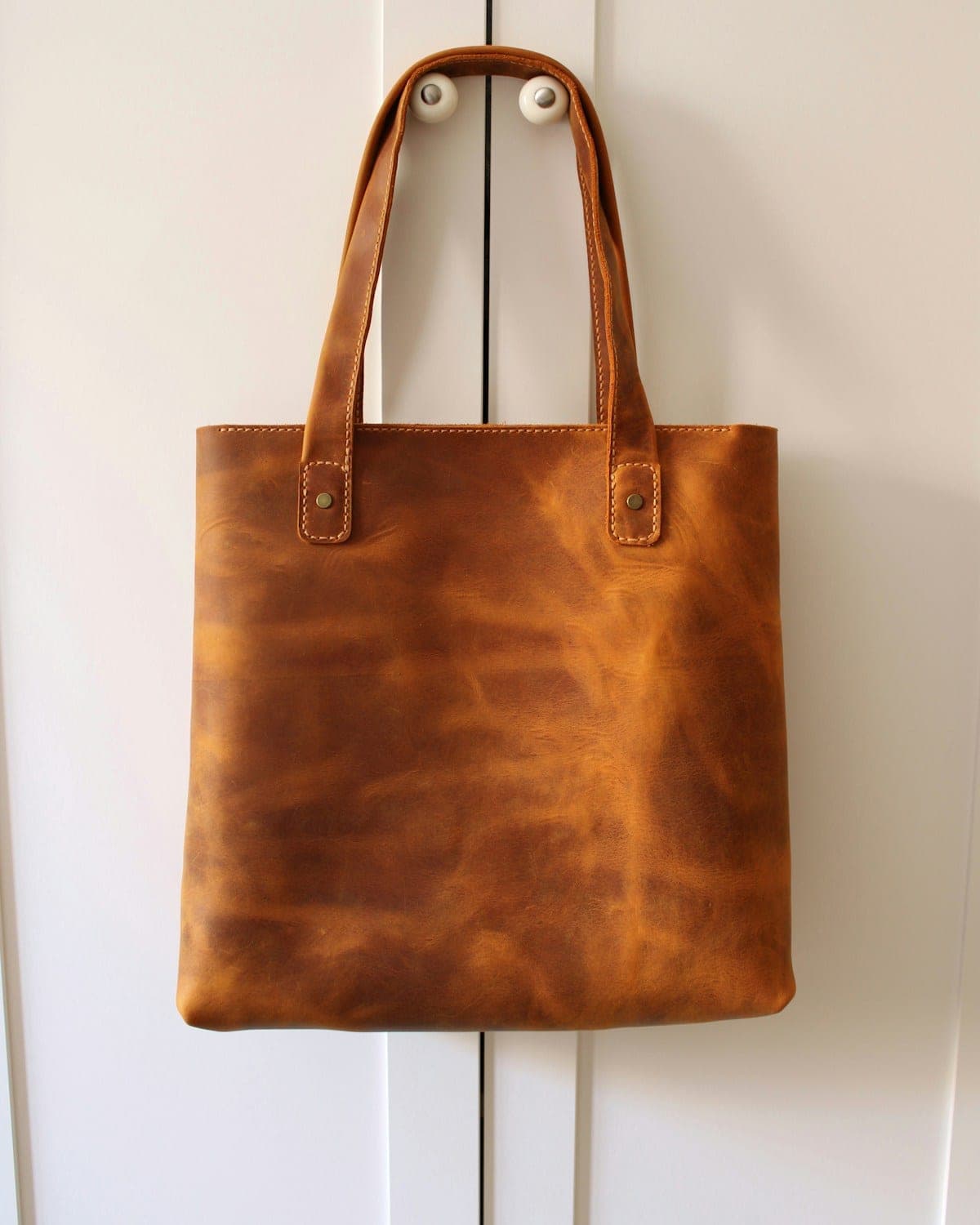 Tan leather tote bag hanging on a wall