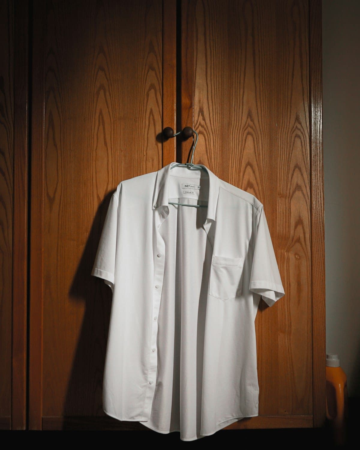 White short-sleeved shirt hanging on a wooden wardrobe