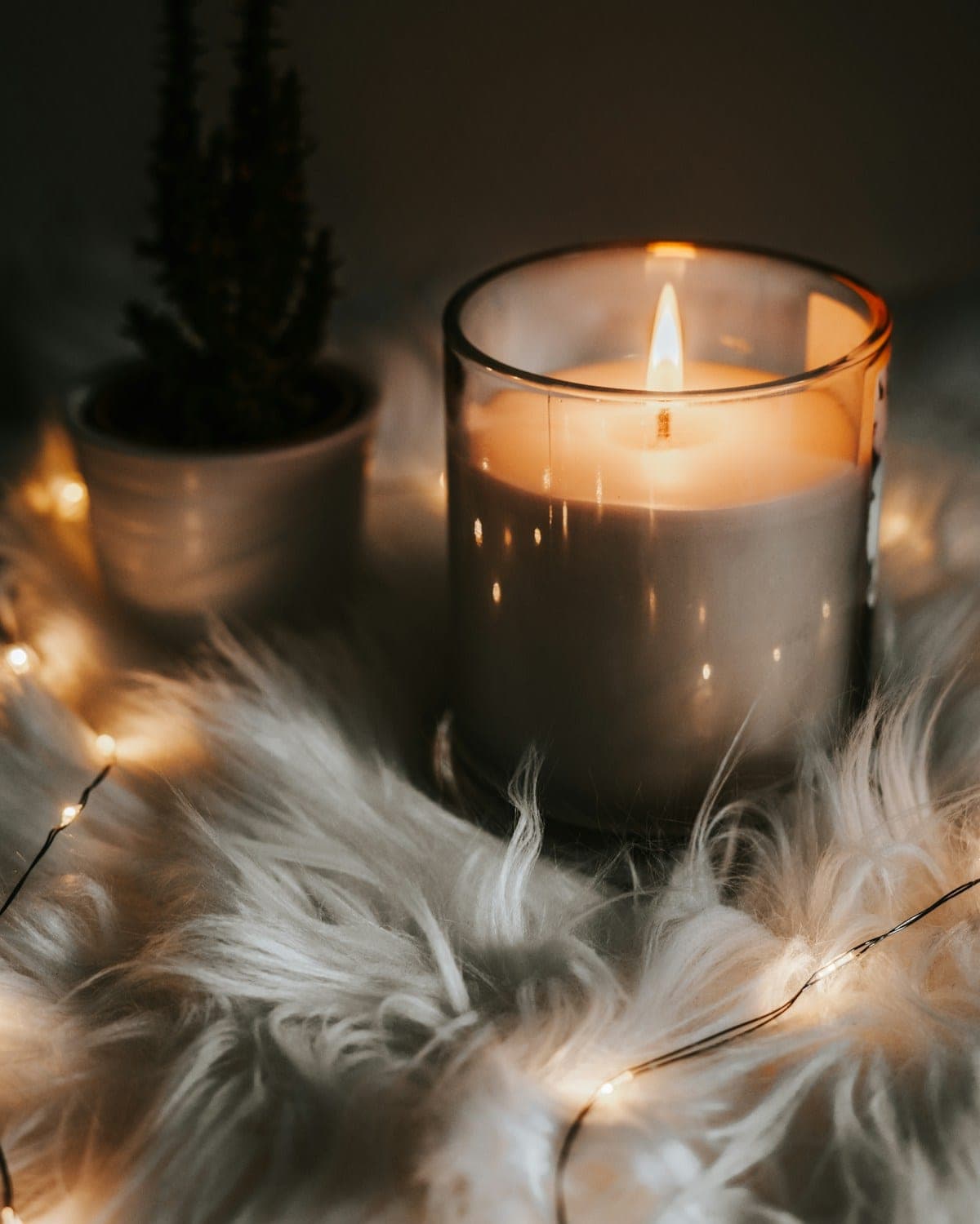 Lit candle in a glass jar beside soft sheepskin