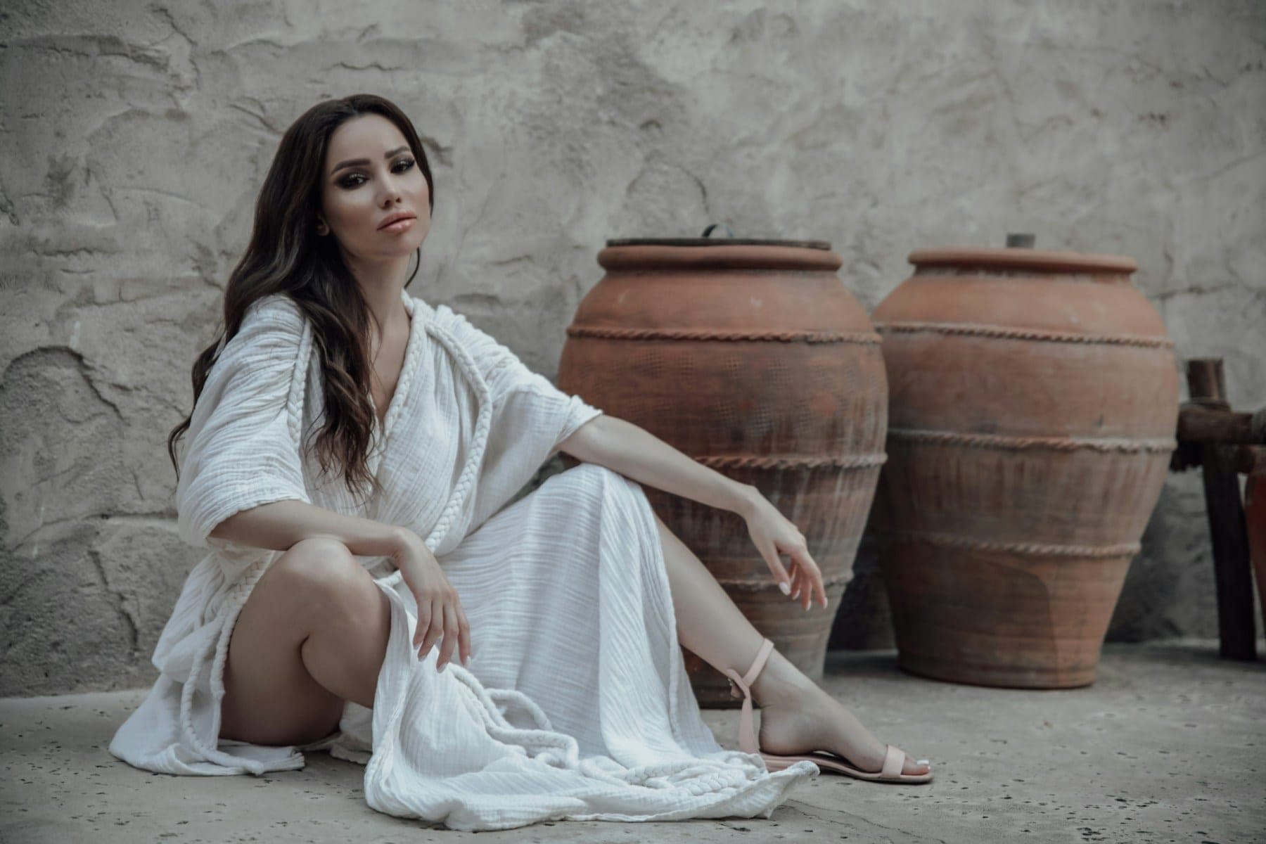 Woman in a flowing white dress seated beside terracotta pots